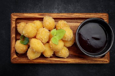 Tahta tahtada tatlı soslu peynirli nugget topları, koyu arkaplanda.