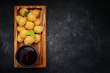 Tahta tahtada tatlı soslu peynirli nugget topları, koyu arkaplanda.