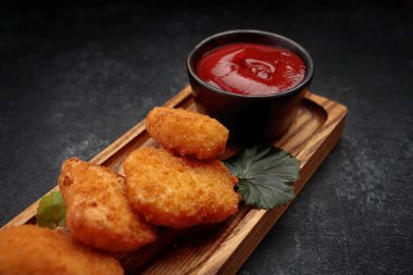 Koyu arkaplanda ketçaplı et parçaları, ahşap bir yüzey üzerinde.