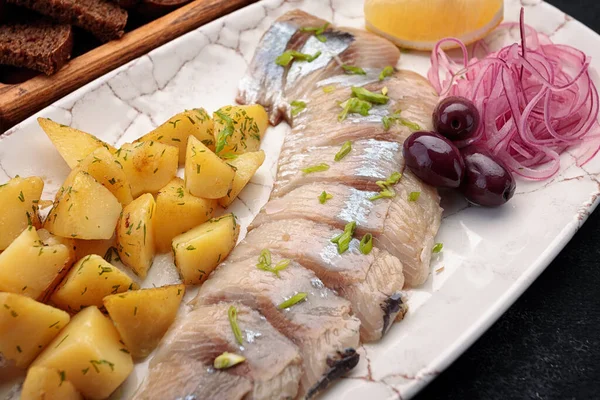 Tuzlu ringa balığı, patates, soğan, zeytin, limon ve tost, koyu bir arka planda.
