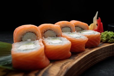 Sushi rulo Philadelphia, wasabi ve zencefil ile, bir ahşap tahta üzerinde bir yaprak bambu ile, koyu bir arka plan