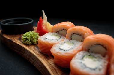 Sushi rulo Philadelphia, wasabi ve zencefil ile, bir ahşap tahta üzerinde bir yaprak bambu ile, koyu bir arka plan
