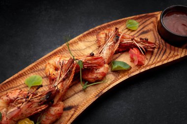 Sarımsak soslu ızgara karides, ahşap bir tahtada, koyu bir arka planda.