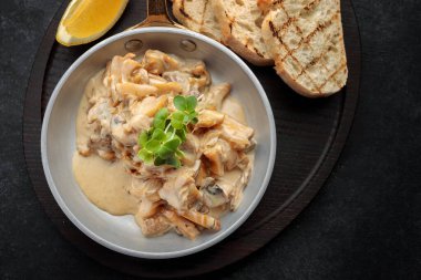 Limonlu ve tostlu krema soslu Rapani kızartma tavasında, siyah arka planda.