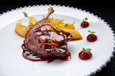 Karamelli ördek bacağı, beyaz bir tabakta, siyah bir arka planda.