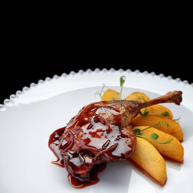 Karamelli ördek bacağı, beyaz bir tabakta, siyah bir arka planda.