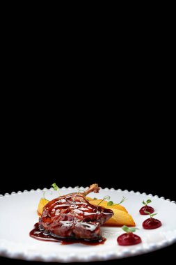 Karamelli ördek bacağı, beyaz bir tabakta, siyah bir arka planda.