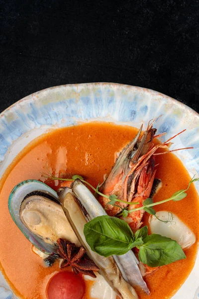 Deniz mahsullü Bouillabaisse çorbası, midye, karides, kalamar. Bir tabakta, karanlık bir arka planda.