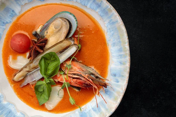 Deniz mahsullü Bouillabaisse çorbası, midye, karides, kalamar. Bir tabakta, karanlık bir arka planda.