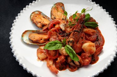 Beyaz bir tabakta karides, midye, kalamar ve deniz tarağı ile sotelenmiş deniz ürünleri.