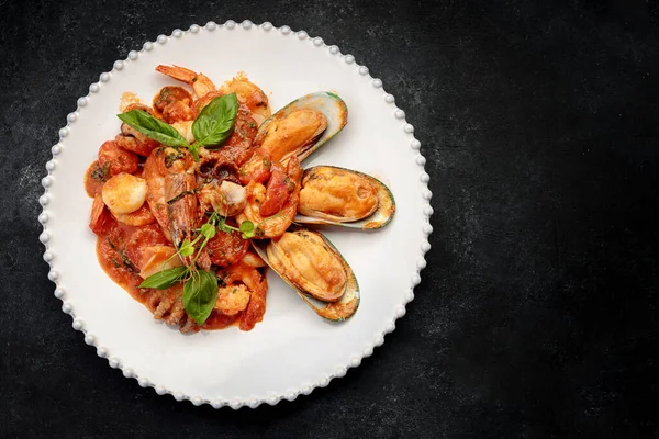 Beyaz bir tabakta karides, midye, kalamar ve deniz tarağı ile sotelenmiş deniz ürünleri.