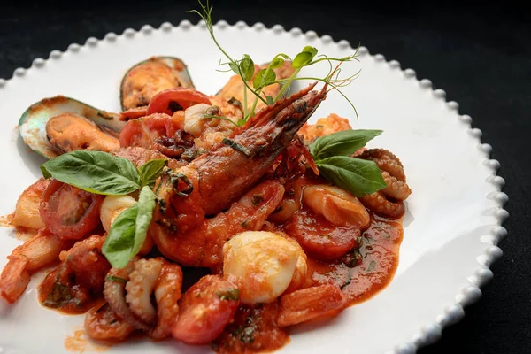 Beyaz bir tabakta karides, midye, kalamar ve deniz tarağı ile sotelenmiş deniz ürünleri.