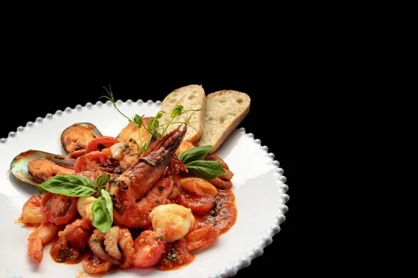 Beyaz bir tabakta karides, midye, kalamar ve deniz tarağı ile sotelenmiş deniz ürünleri.