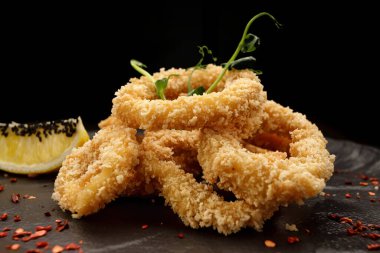 Kızarmış soğan halkaları, baharatlı, siyah bir tabakta, siyah bir arka planda.