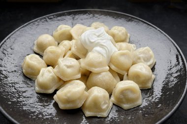 Ekşi kremalı Ukrayna hamur tatlısı, siyah parlak bir tabakta, koyu bir arka planda.