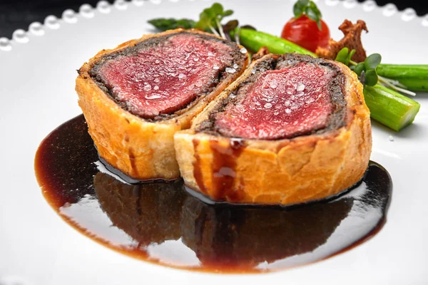 Beef Wellington with chanterelles, asparagus and black truffle with spicy Razmarin sauce, on a black background