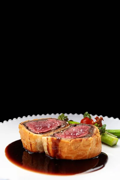 Beef Wellington with chanterelles, asparagus and black truffle with spicy Razmarin sauce, on a black background