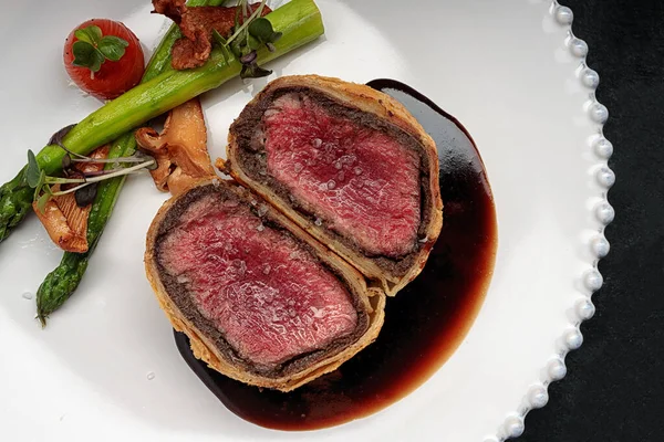 Beef Wellington with chanterelles, asparagus and black truffle with spicy Razmarin sauce, on a black background