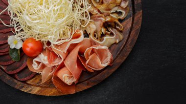 Bira, kurutulmuş mürekkep balığı, basturma, jamon, domuz kulağı ve vişneli domates seti, koyu bir arka planda.