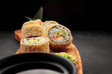 Banzai suşisi, soya soslu, tahta tahtada, karanlık bir arka planda.