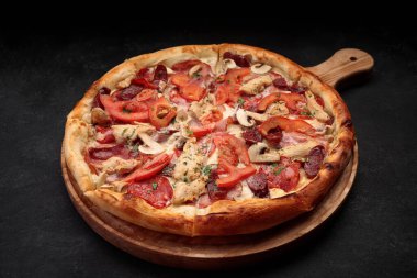 Tavuk, mantar, sosis, et ve domatesli pizza. Tahtanın üzerinde, karanlık bir arka planda.