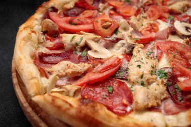 Tavuk, mantar, sosis, et ve domatesli pizza. Tahtanın üzerinde, karanlık bir arka planda.