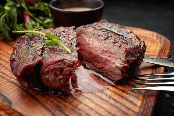 Meat steak on the wooden board, on a dark background