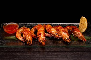 Soslu ve limonlu ızgara karides, siyah arka planda.
