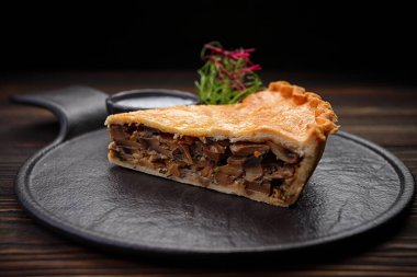 Ahşap bir arka planda, mantarlı ve soslu bir parça fırında turta.