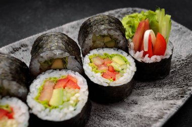 Suşi Yasai 'yi bir tabakta yuvarlıyor, karanlık bir arka planda.