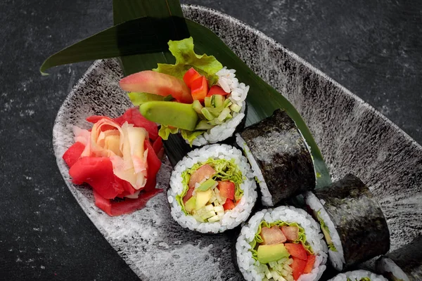 Suşi Yasai 'yi bir tabakta yuvarlıyor, karanlık bir arka planda.