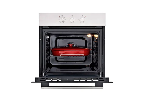 Black oven with silver control panel, three round control knobs. Open door, with a red baking dish, inside lights on. Front view. Isolate on white — Foto de Stock