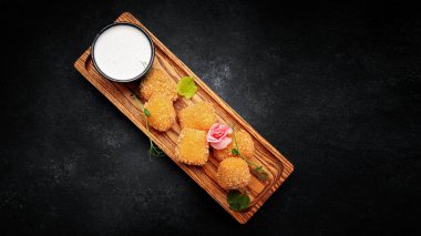 Koyu bir arka planda, ahşap bir tahtada soslu Camembert kızartması.