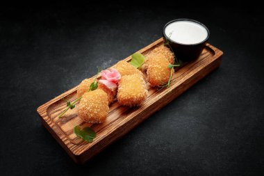 Koyu bir arka planda, ahşap bir tahtada soslu Camembert kızartması.