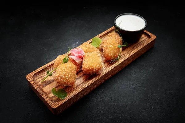 Koyu bir arka planda, ahşap bir tahtada soslu Camembert kızartması.