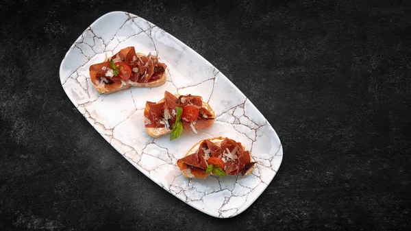 Bruschetta con parma y salsa, en un plato, sobre un fondo oscuro —  Fotos de Stock