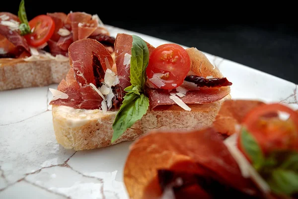 Bruschetta with parma and sauce, on a plate, on a dark background — Stock Photo, Image