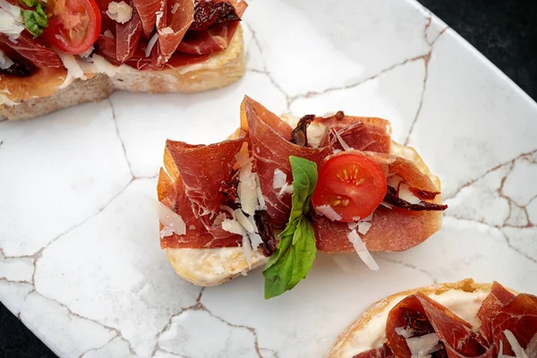 Bruschetta with parma and sauce, on a plate, on a dark background — Stock Photo, Image