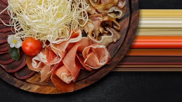 Bira, kurutulmuş mürekkep balığı, basturma, jamon, domuz kulağı ve vişneli domates seti, koyu bir arka planda.