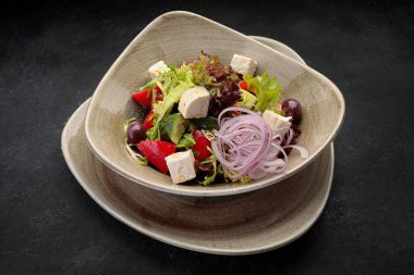 Peynirli taze sebze salatası, bir tabakta, koyu bir arka planda.