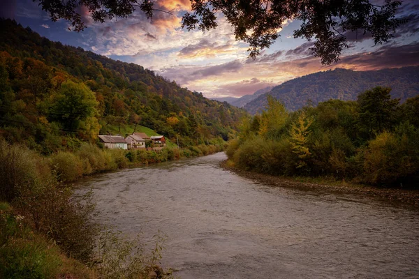 Mystical river in the mountains and village houses on the shore, at sunset