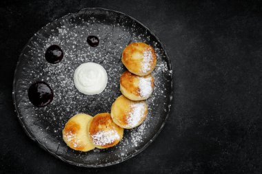 Ekşi kremalı, siyah tabakta süzme peynirli kekler.