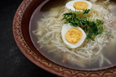 Koyu bir arka planda, vermicelli, otlu ve yumurtalı tavuk suyu çorbası.