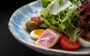 Ton balıklı Nicoise salatası, bir tabakta, koyu arkaplanda.