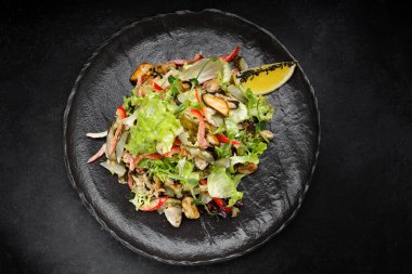 Kızarmış midye ve turşulu salata, siyah tabakta.