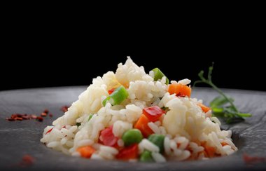 Siyah bir arka planda, siyah bir tabakta sebze ve baharatlı risotto.