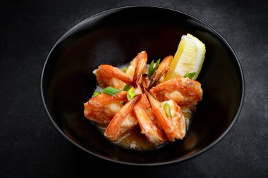 Siyah tabakta limonlu soslu kızarmış karides.