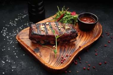 Izgara domuz pirzolası, barbekü sosu ve roka ile karamelize edilmiş. Koyu beton arka planda servis yapmak için ahşap bir tahtanın üzerinde lezzetli bir bira aperatifi.