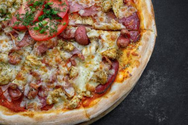 Sosisli, tavuklu, peynirli ve domatesli pizza gri beton arka planda, seçici bir odak ile. Yatay