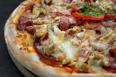 Sosisli, tavuklu, peynirli ve domatesli pizza gri beton arka planda, seçici bir odak ile. Yatay